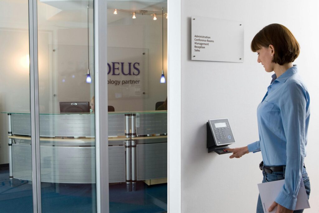 Woman using biometric scanner in modern office setting for access control.